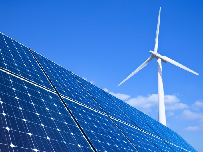 Solar panels and wind turbine against blue sky